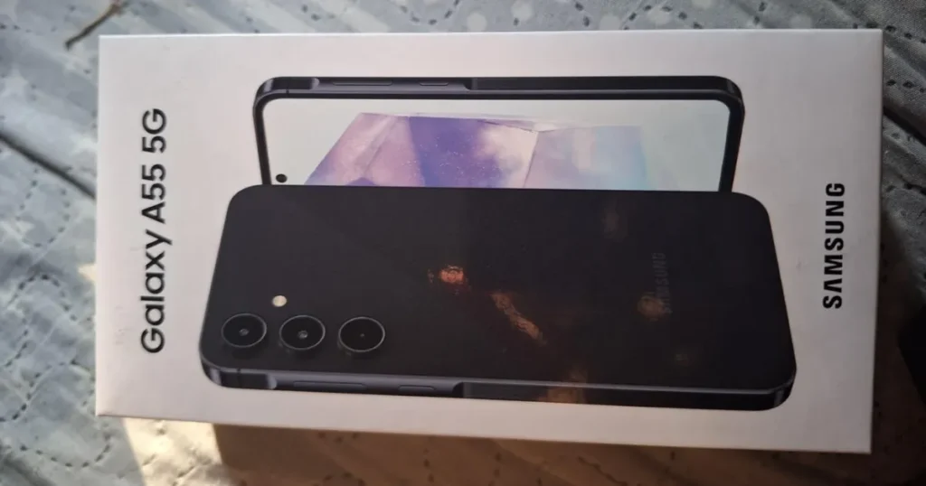 Fotografia da caixa do smartphone Samsung Galaxy A55 5G. A embalagem é branca e exibe uma imagem do aparelho na cor preta, deitado sobre uma superfície de tecido.