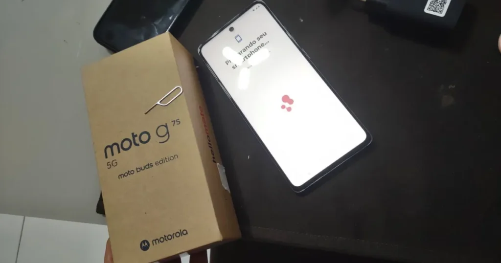 Fotografia de uma caixa e um celular de um suposto "Moto G75 5G", que é um modelo não oficial. O celular está no processo de inicialização e a caixa indica ser uma "moto buds edition".