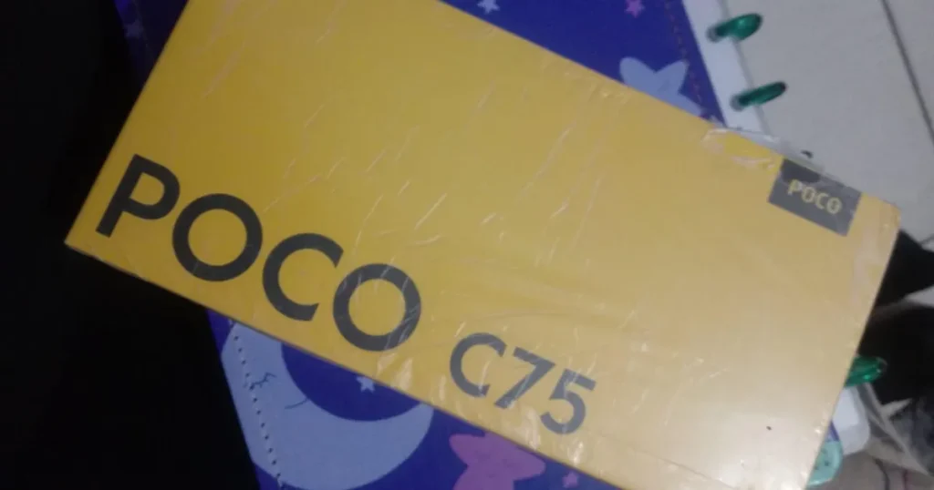 Fotografia da caixa amarela de um suposto smartphone "Poco C75". A embalagem, que aparenta ser uma falsificação, está selada com plástico sobre um caderno.