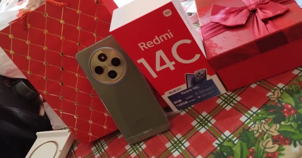 Foto de um celular e uma caixa falsificados, ambos rotulados como "Redmi 14C". O aparelho, que tem um design de conceito, e sua caixa vermelha estão ao lado de embalagens de presente.
